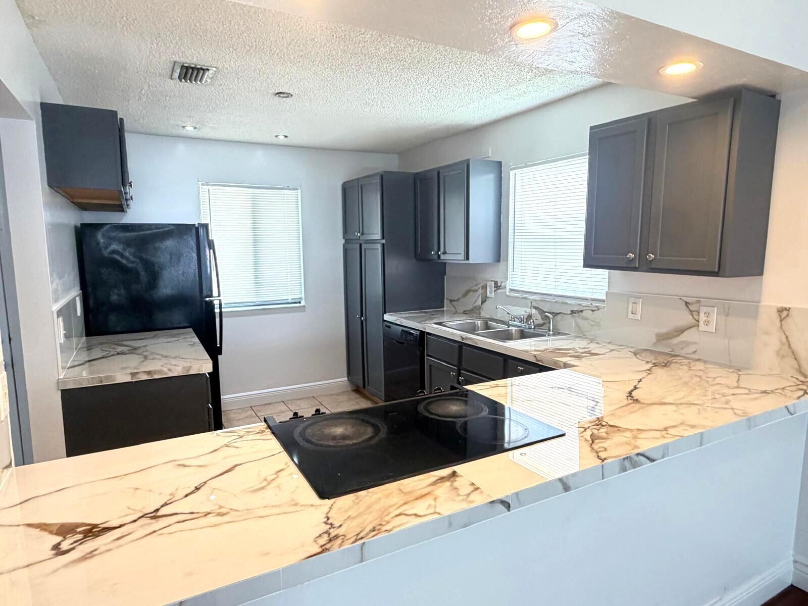 A kitchen features dark gray cabinets, marble-patterned countertops, and a black glass cooktop — 3808 Inlet Circle # 3808, FL 33463, FL