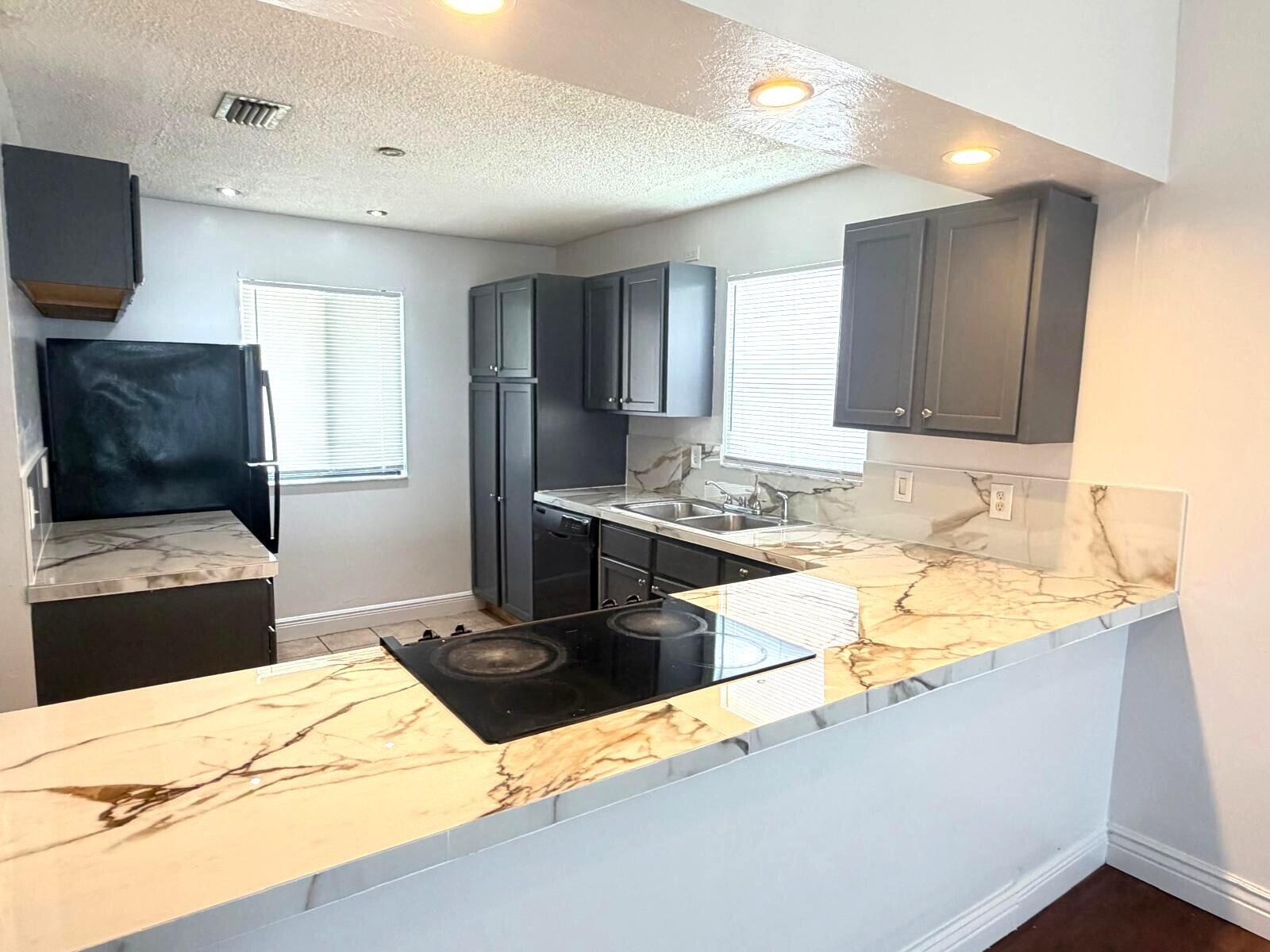 A kitchen features dark gray cabinets, marble-patterned countertops, and a black electric cooktop — 3808 Inlet Circle # 3808, FL 33463, FL