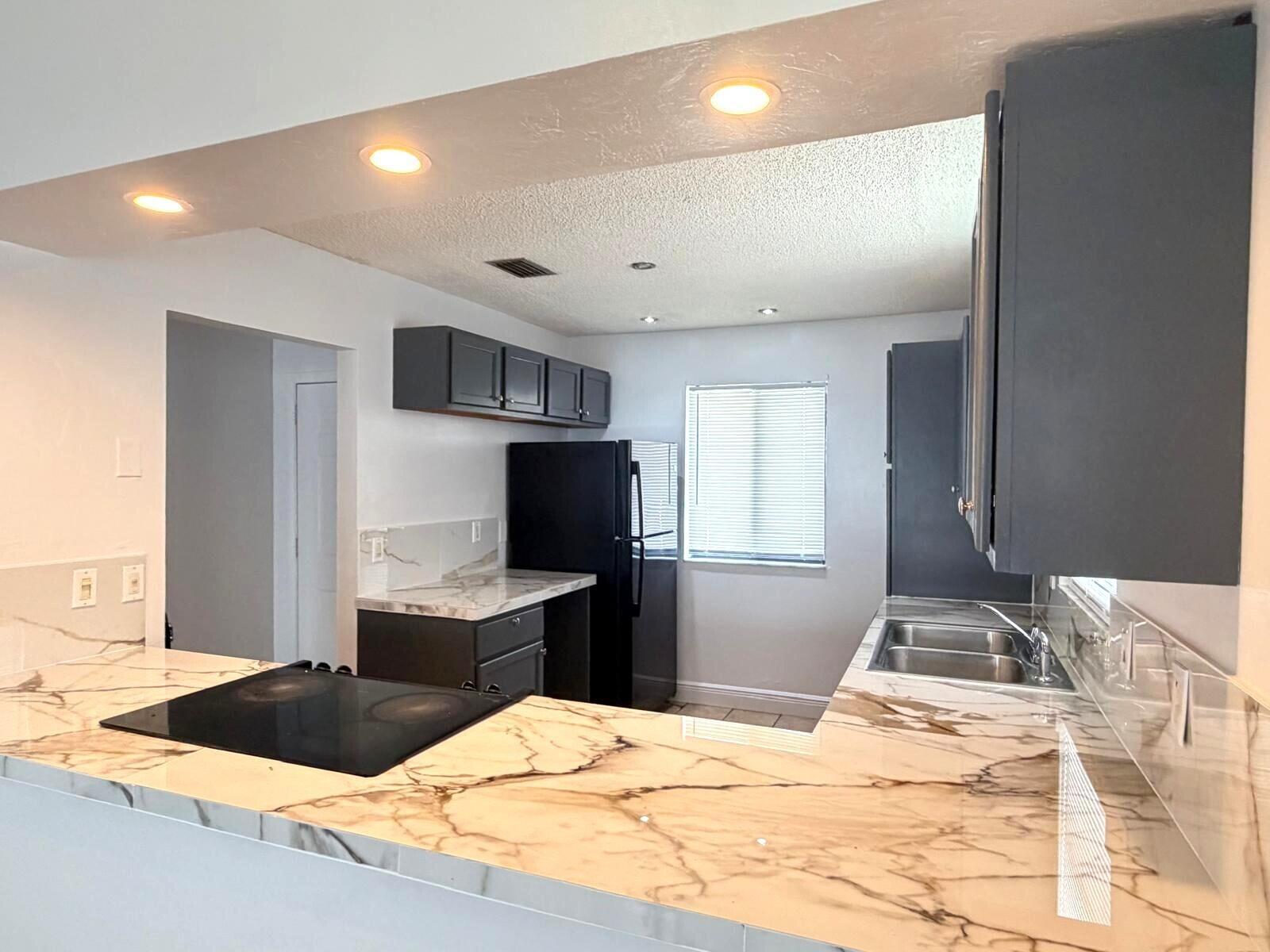 A kitchen features dark gray cabinets, black appliances, and white marble-patterned countertops — 3808 Inlet Circle # 3808, FL 33463, FL