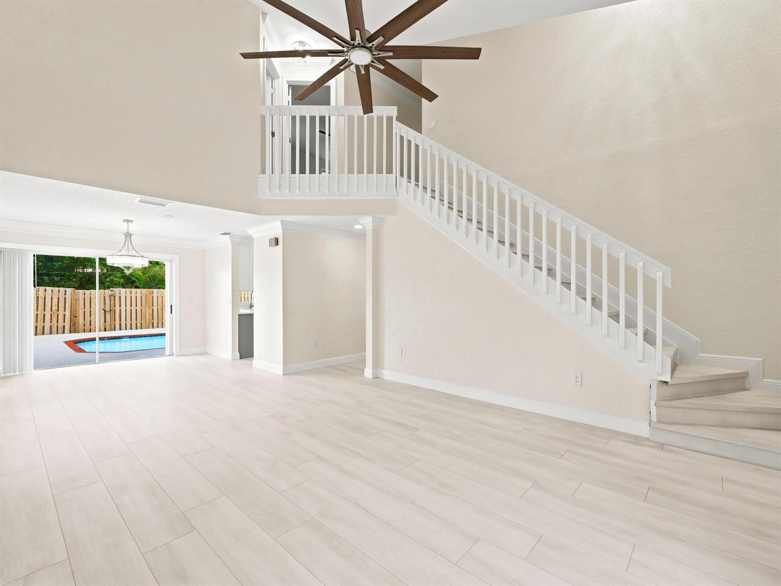An open living area features light wood-look flooring, a staircase with white railings, and a pool — 3157 NW 120th Way, Sunrise FL 33323, SUNRISE, FL