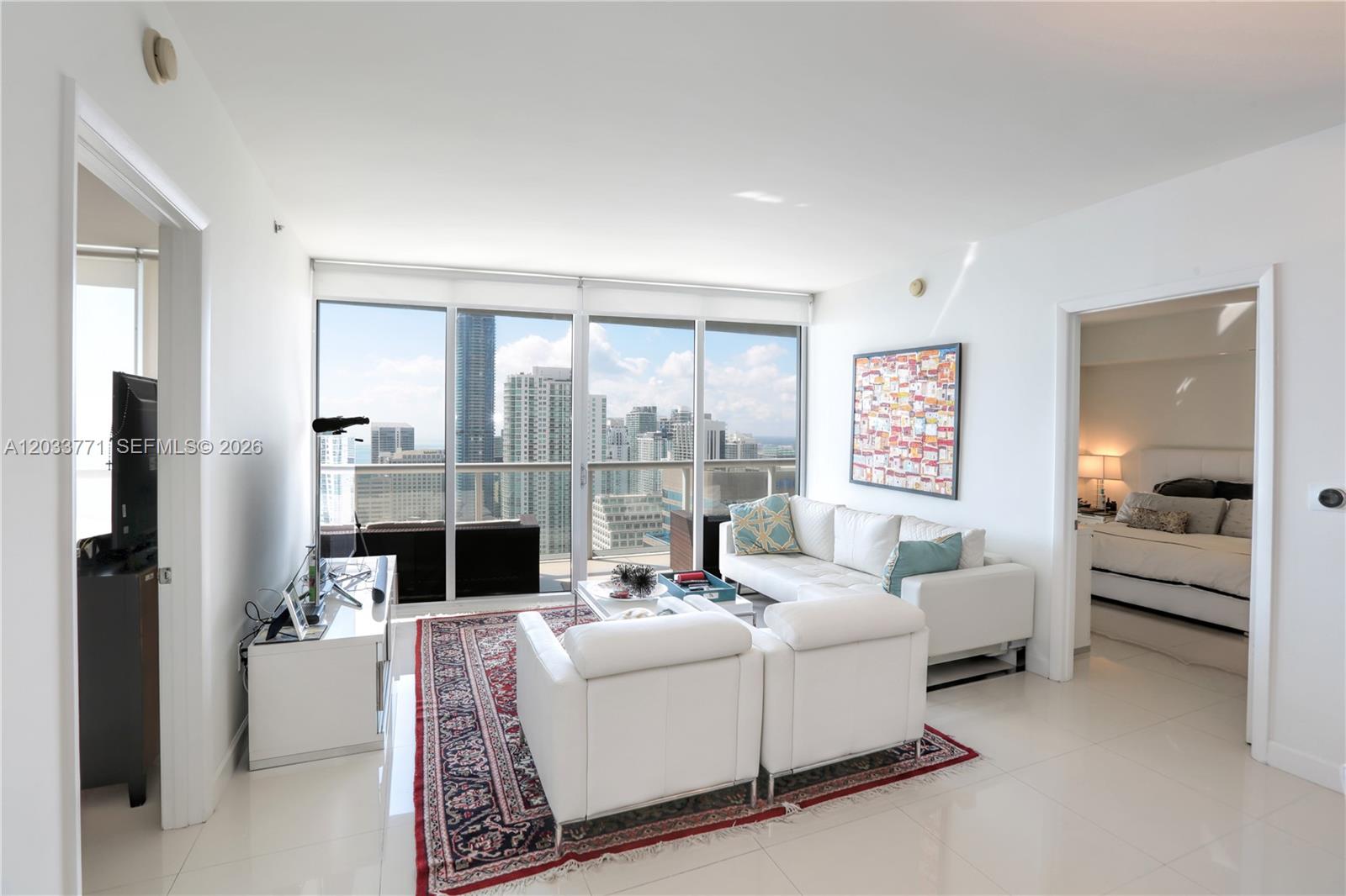 A bright living room features white leather furniture, a patterned rug, and floor-to-ceiling windows — 495 Brickell Ave # 4703, Miami FL 33131, MIAMI, FL