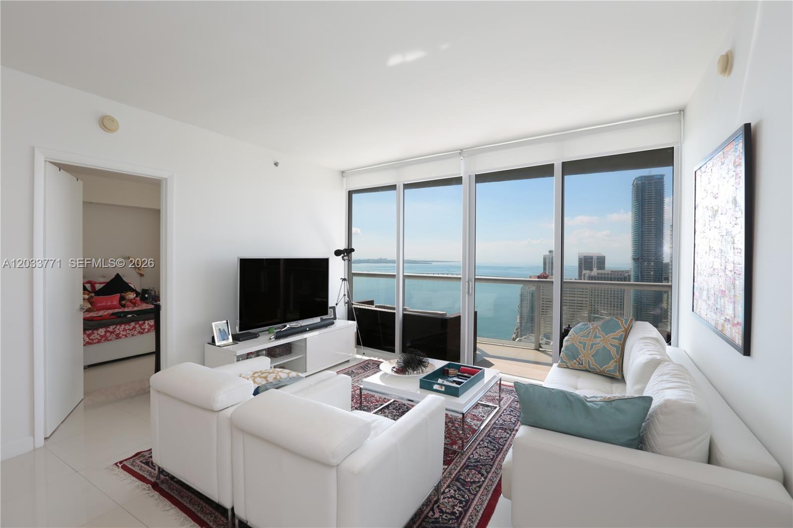 A living room features white furniture, a patterned rug, and floor-to-ceiling windows overlooking the ocean — 495 Brickell Ave # 4703, Miami FL 33131, MIAMI, FL