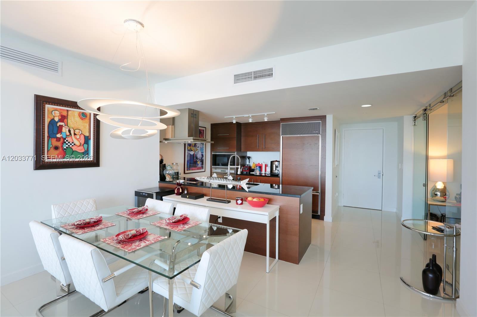 A modern dining area features a glass table, white chairs, and an adjacent open kitchen — 495 Brickell Ave # 4703, Miami FL 33131, MIAMI, FL