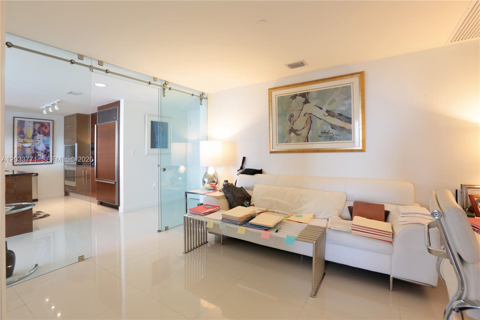 A living room features a white sofa, a metal coffee table, and a glass sliding door — 495 Brickell Ave # 4703, Miami FL 33131, MIAMI, FL
