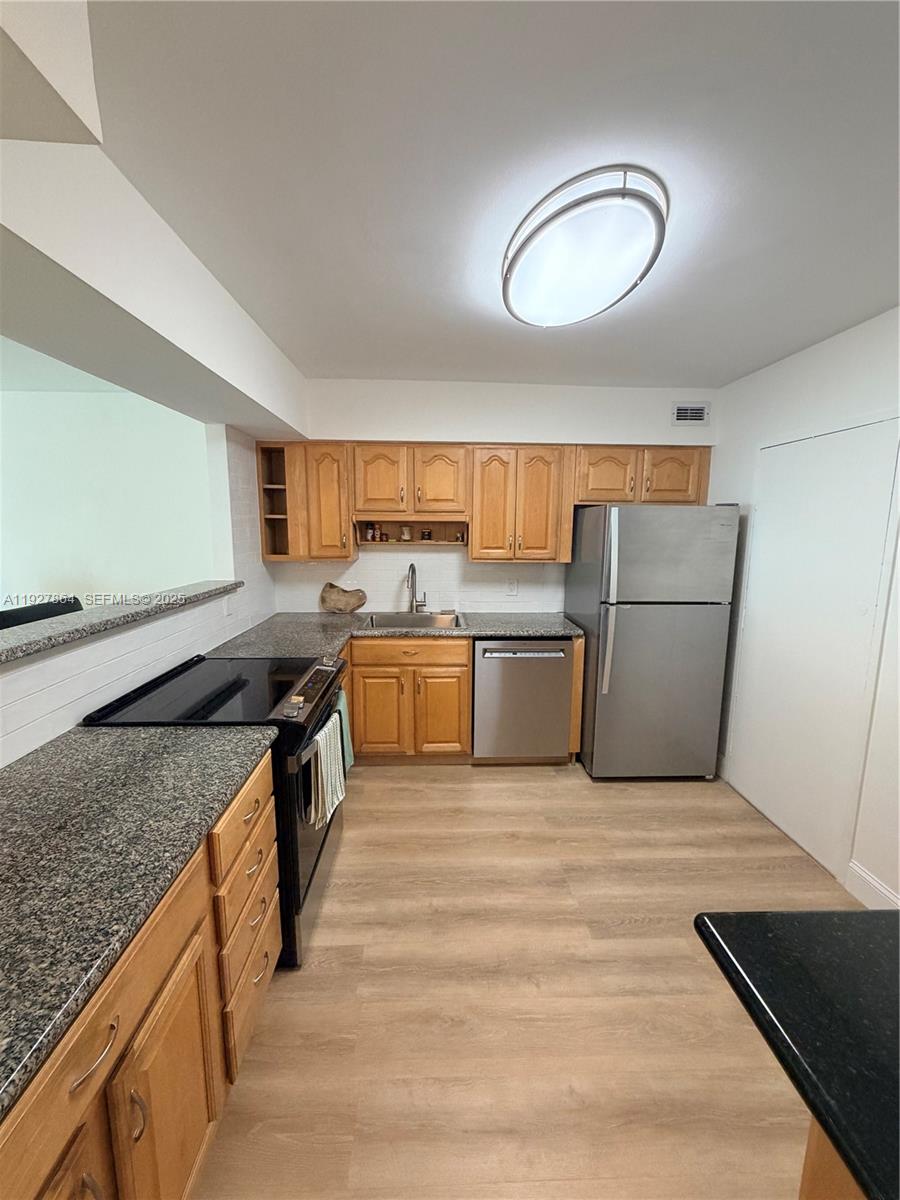 A kitchen features light wood cabinets, granite countertops, stainless steel appliances, and wood-look flooring — 5151 Collins Ave, Miami Beach FL 33140, MIAMI BEACH, FL