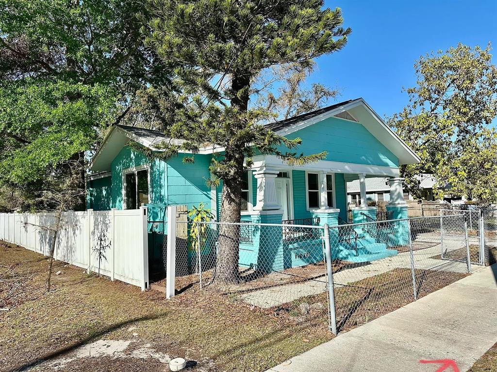 A turquoise bungalow with a front porch and white fence sits behind a chain-link fence — 1504 E 33RD AVENUE, TAMPA, FL