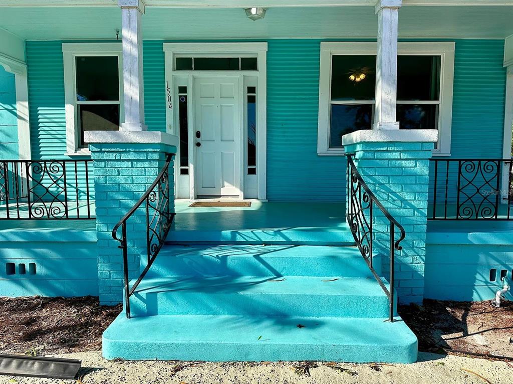 A bright turquoise house exterior features a front porch with brick columns and metal railings — 1504 E 33RD AVENUE, TAMPA, FL
