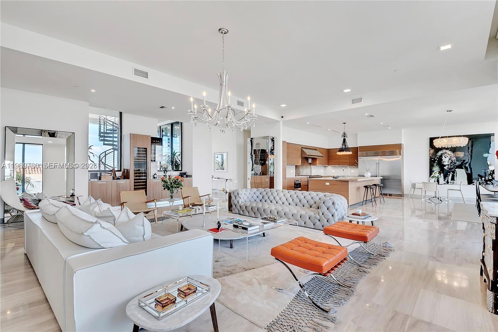 An open-concept living room features a tufted gray sofa, white sectional, and modern kitchen — 3581 E Glencoe St # 605, Coconut Grove FL 33133, COCONUT GROVE, FL