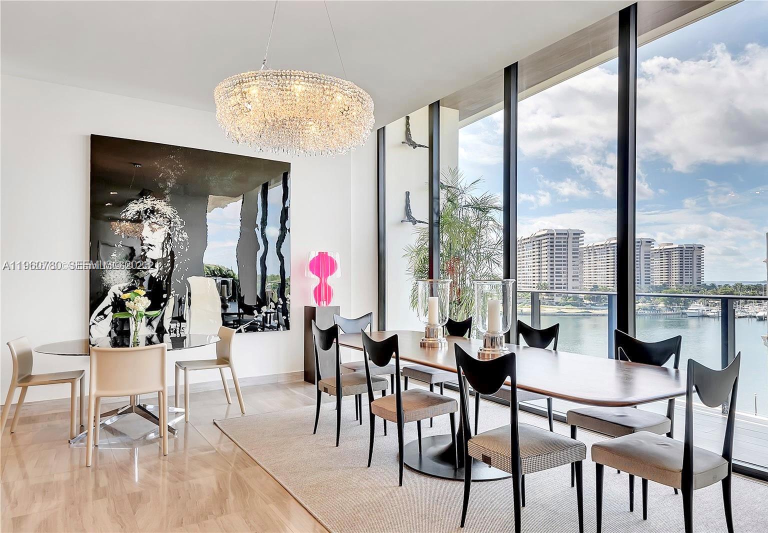 A modern dining room features a large crystal chandelier, abstract wall art, and floor-to-ceiling windows — 3581 E Glencoe St # 605, Coconut Grove FL 33133, COCONUT GROVE, FL