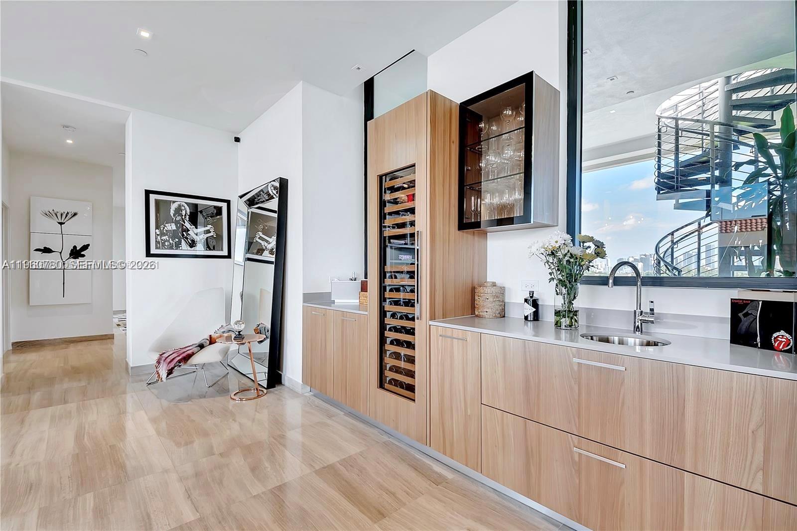 A modern wet bar features light wood cabinetry, a wine cooler, and a spiral staircase outside — 3581 E Glencoe St # 605, Coconut Grove FL 33133, COCONUT GROVE, FL