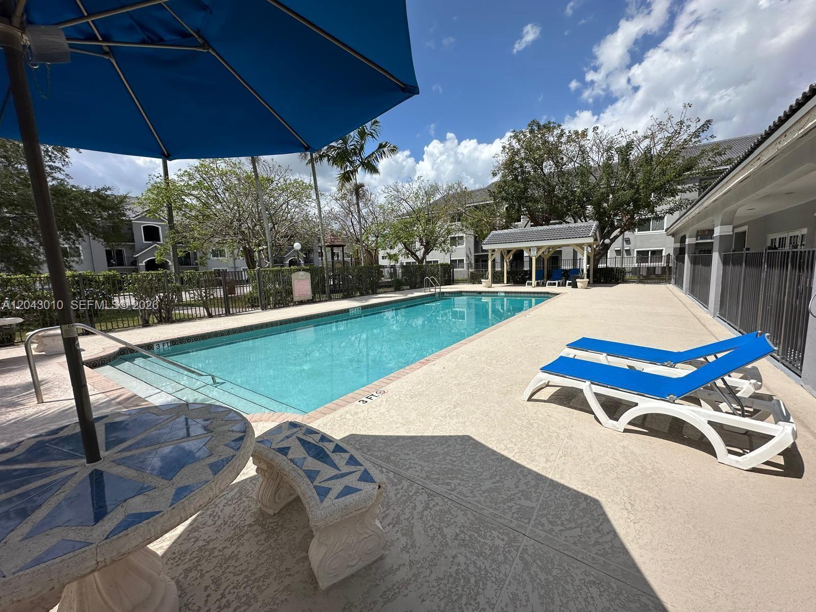An outdoor swimming pool area features lounge chairs, a tiled table, and a covered gazebo — HOMESTEAD, FL