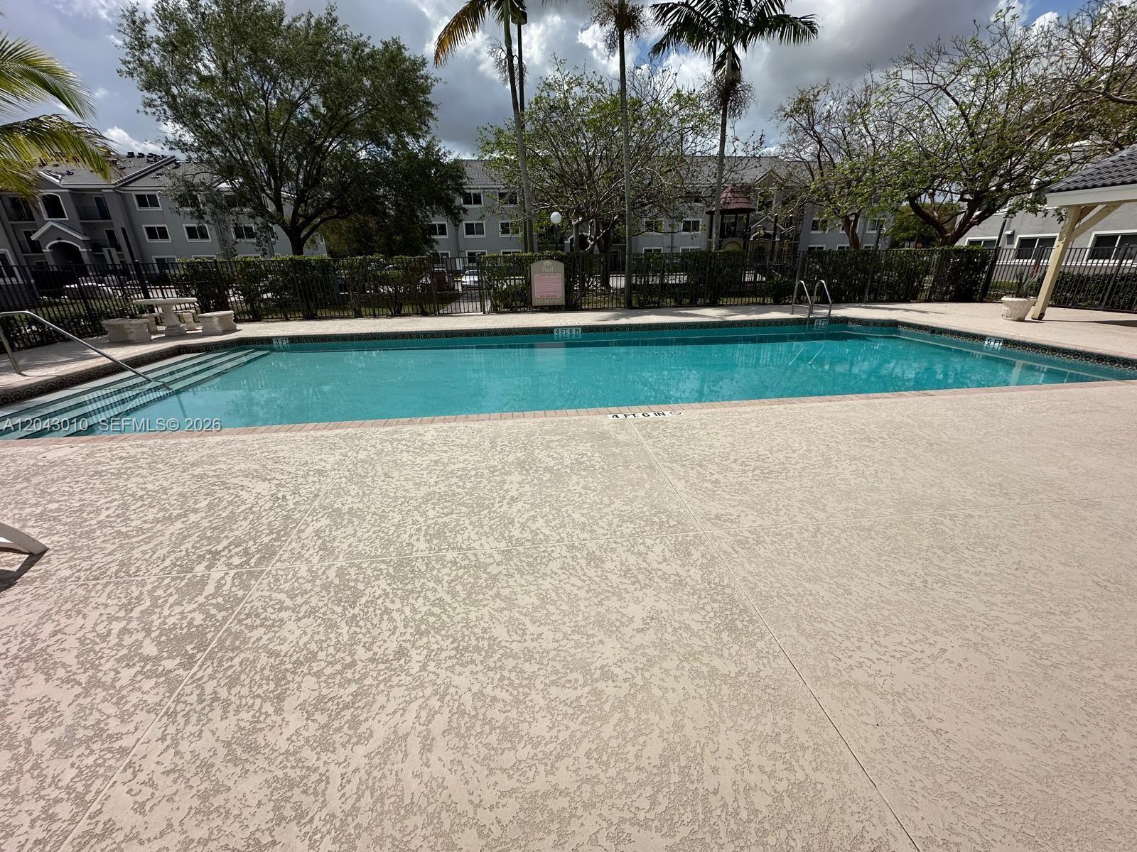 An outdoor swimming pool with a concrete deck is surrounded by a black metal fence — HOMESTEAD, FL