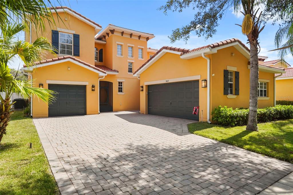 A two-story yellow stucco house features a paved driveway and two dark gray garage doors — 3827 GOLDEN KNOT DRIVE, KISSIMMEE, FL