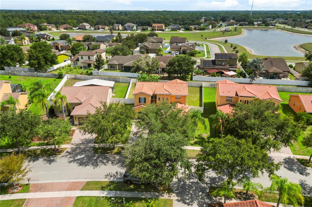 An aerial view shows a suburban neighborhood with several houses, green lawns, and a lake — 3827 GOLDEN KNOT DRIVE, KISSIMMEE, FL
