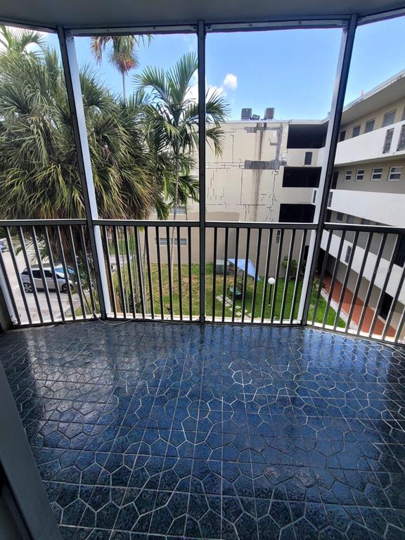 A screened-in balcony with dark patterned tile flooring overlooks a courtyard and apartment building — 1690 NE 191TH STREET UNIT 315, MIAMI, FL