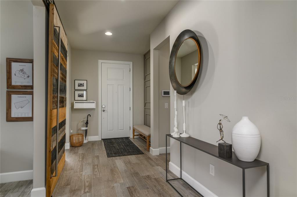 A modern entryway features a wood-paneled sliding door, a console table, and a round mirror — 12203 SEABROOK AVENUE, BRADENTON, FL