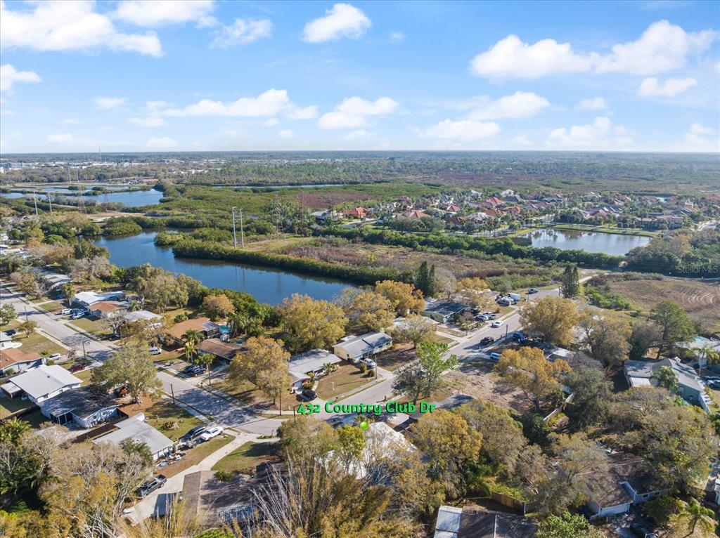 An aerial view shows a residential neighborhood with houses, trees, and a nearby lake — 432 COUNTRY CLUB DRIVE, OLDSMAR, FL