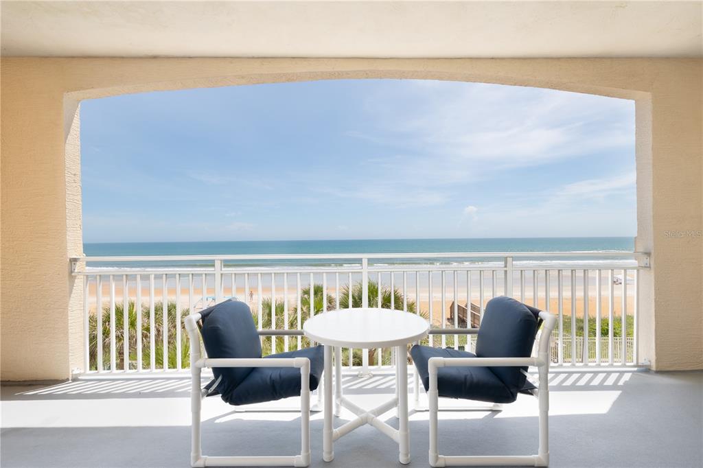 A balcony with two chairs and a table overlooks the ocean and sandy beach — 1425 OCEAN SHORE BOULEVARD UNIT 203, ORMOND BEACH, FL