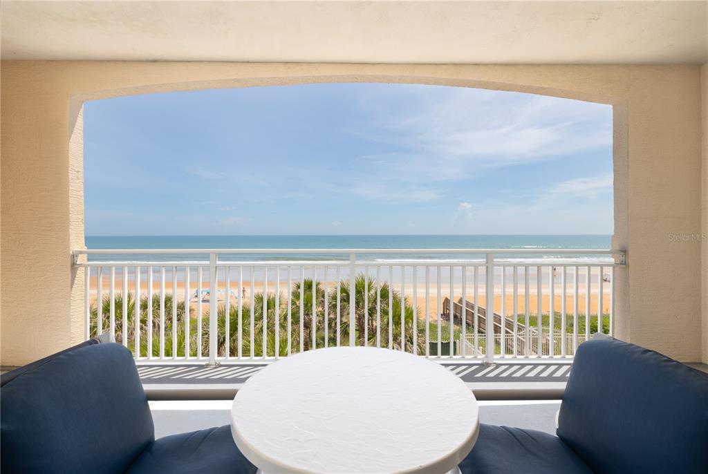 A balcony with two chairs and a table overlooks a sandy beach and the ocean — 1425 OCEAN SHORE BOULEVARD UNIT 203, ORMOND BEACH, FL