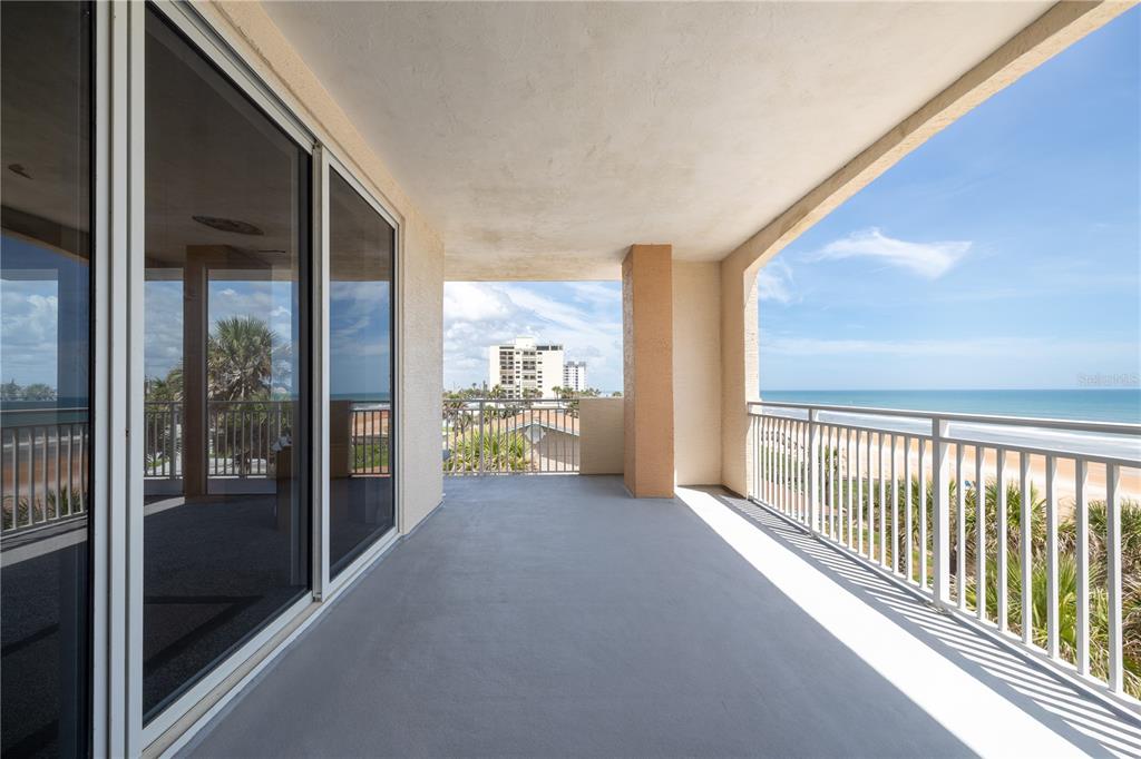 A spacious covered balcony features a concrete floor, white railings, and a direct ocean view — 1425 OCEAN SHORE BOULEVARD UNIT 203, ORMOND BEACH, FL