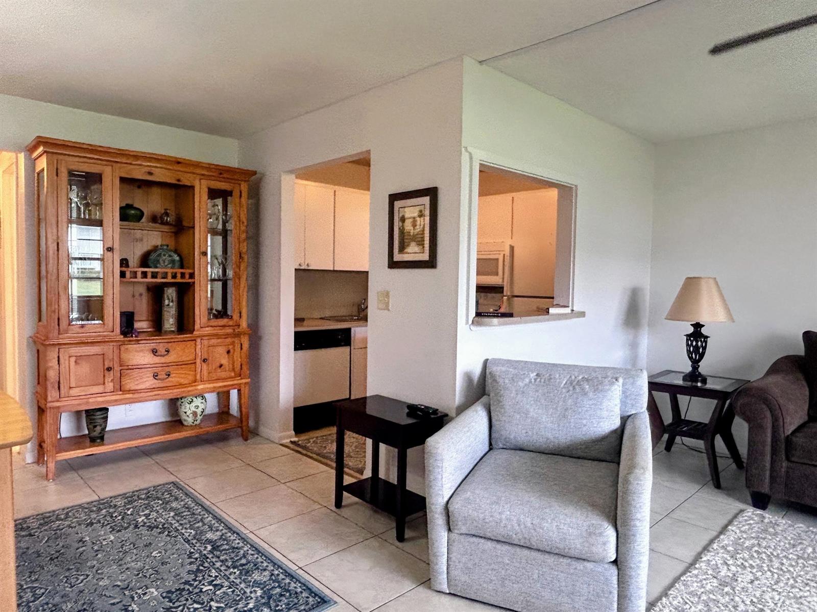 A living room with a wooden hutch, a gray armchair, and a kitchen pass-through window — 680 W Horizons W # 103, Boynton Beach FL 33435, BOYNTON BEACH, FL