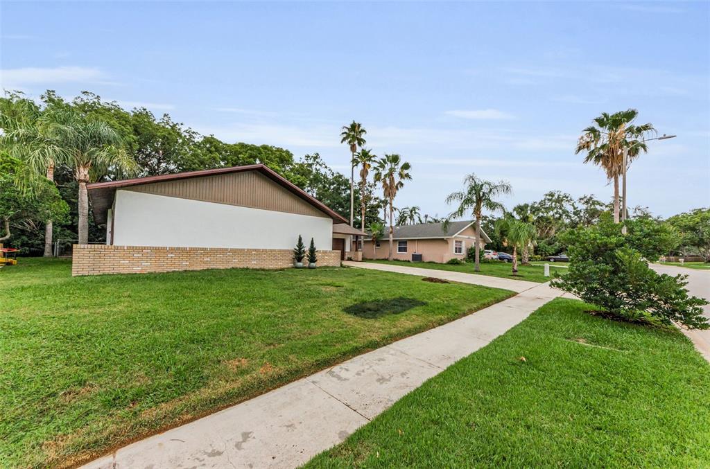 A side view of a house with a brick base, white walls, and a long driveway — 1558 COTTONWOOD TERRACE, DUNEDIN, FL