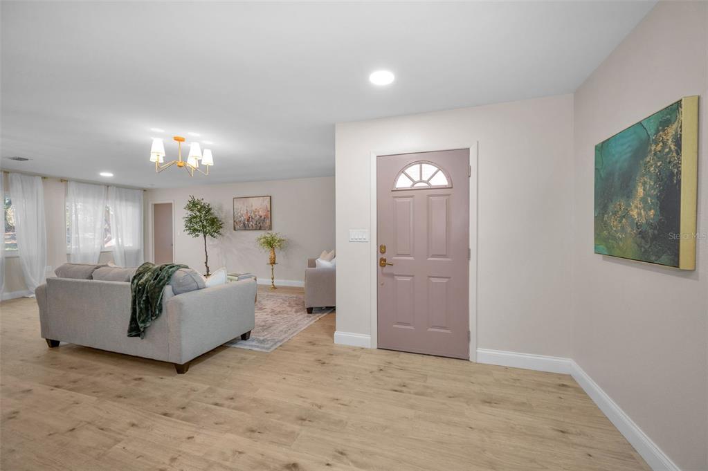 A living room features light wood flooring, a mauve front door, and neutral wall paint — 1558 COTTONWOOD TERRACE, DUNEDIN, FL