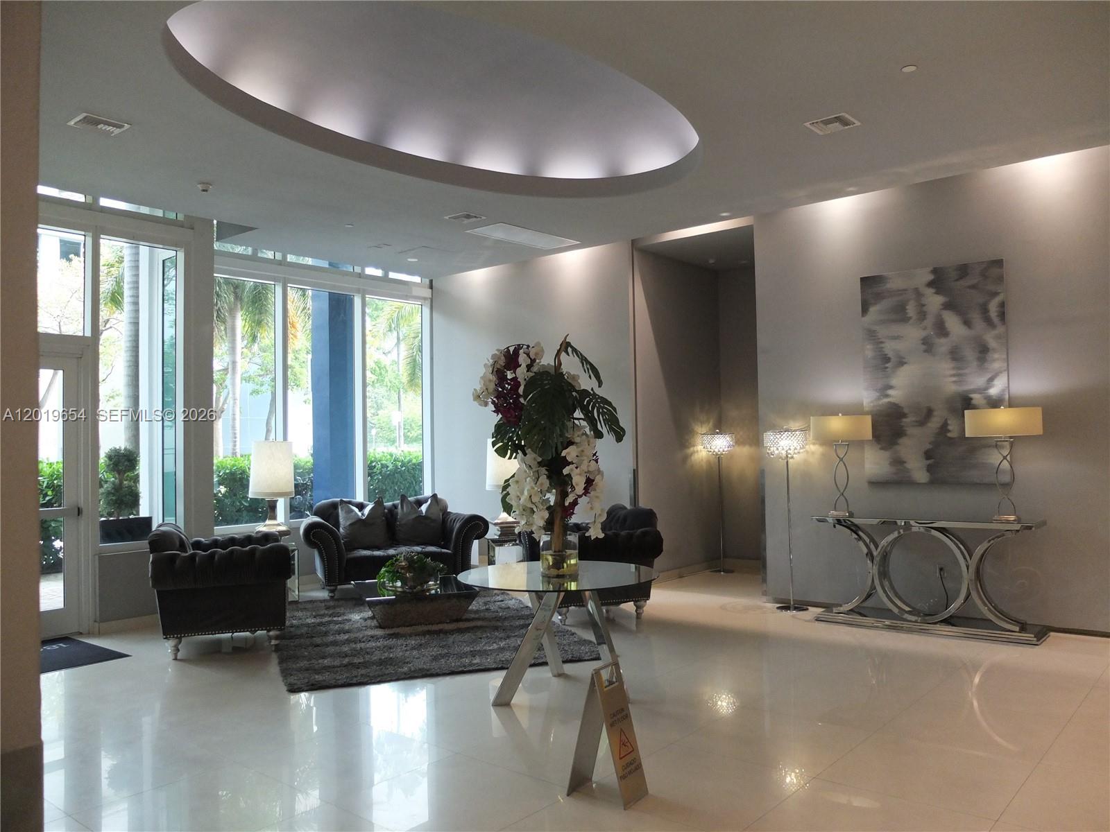 A modern lobby features a circular recessed ceiling light, plush seating, and a glass-topped table — 275 NE 18th St # 1101, Miami FL 33132, MIAMI, FL
