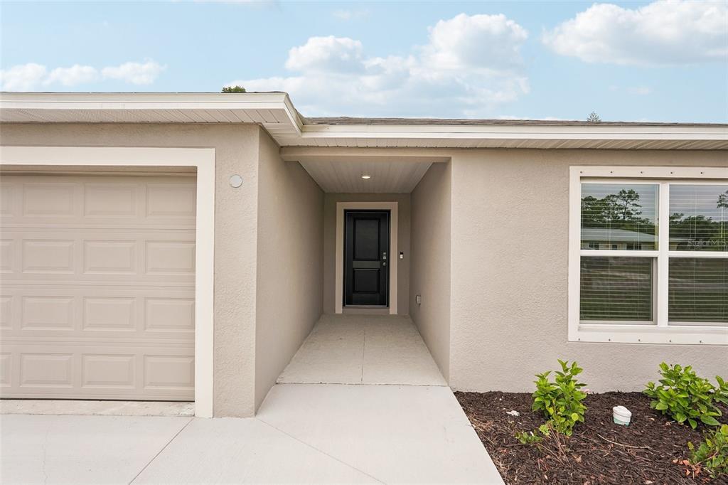 A beige house exterior features a garage, a recessed entryway with a black door, and windows — 20247 ANDOVER AVENUE, PORT CHARLOTTE, FL
