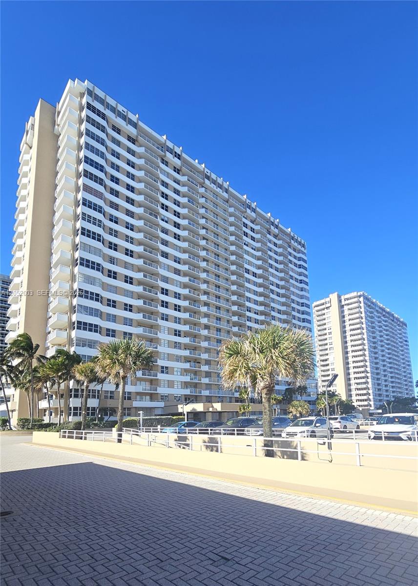 A tall residential apartment building stands behind a paved parking lot with palm trees — 1980 S Ocean Dr # 4L, Hallandale Beach FL 33009, HALLANDALE BEACH, FL