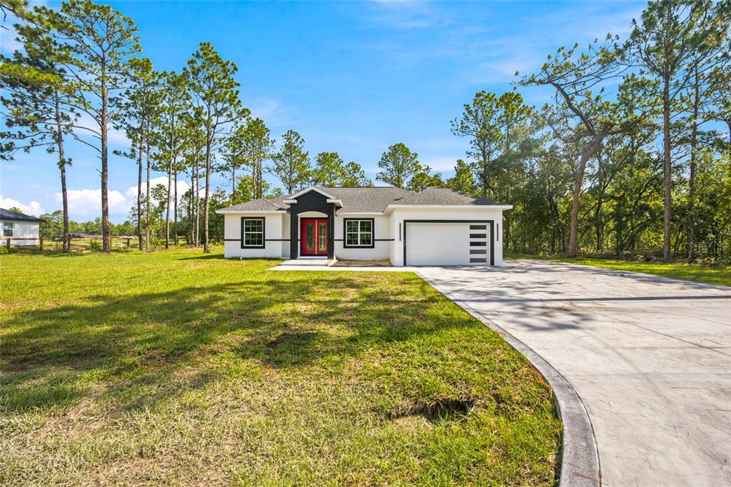 A single-story white house with a red front door, black trim, and a concrete driveway — 12669 SW 81ST STREET, DUNNELLON, FL