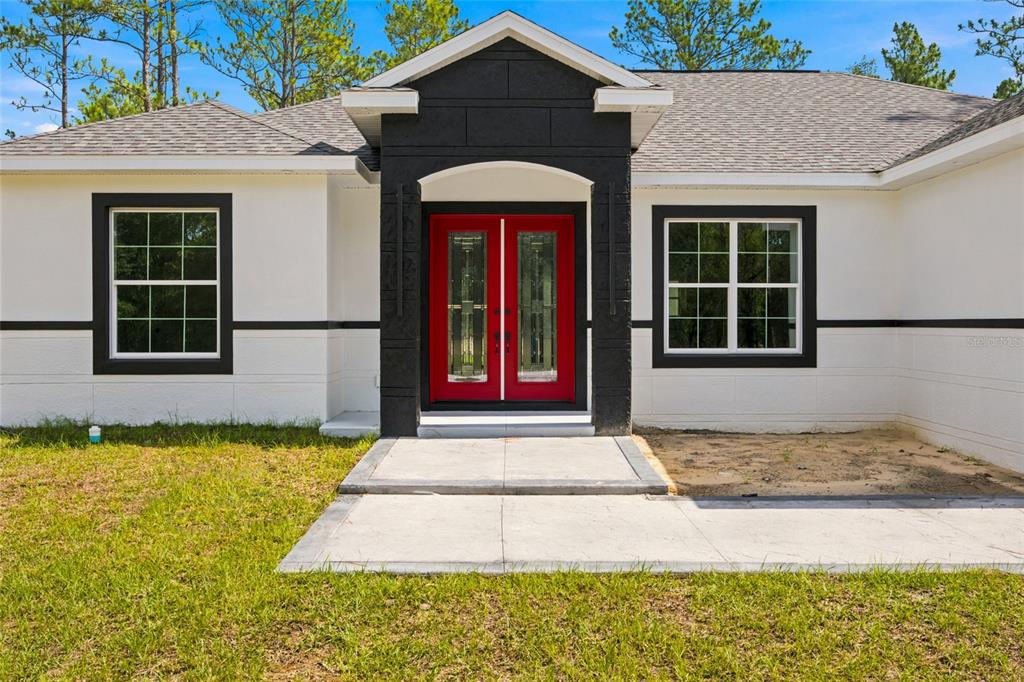 A white house exterior features a black entryway, a bright red double door, and windows — 12669 SW 81ST STREET, DUNNELLON, FL