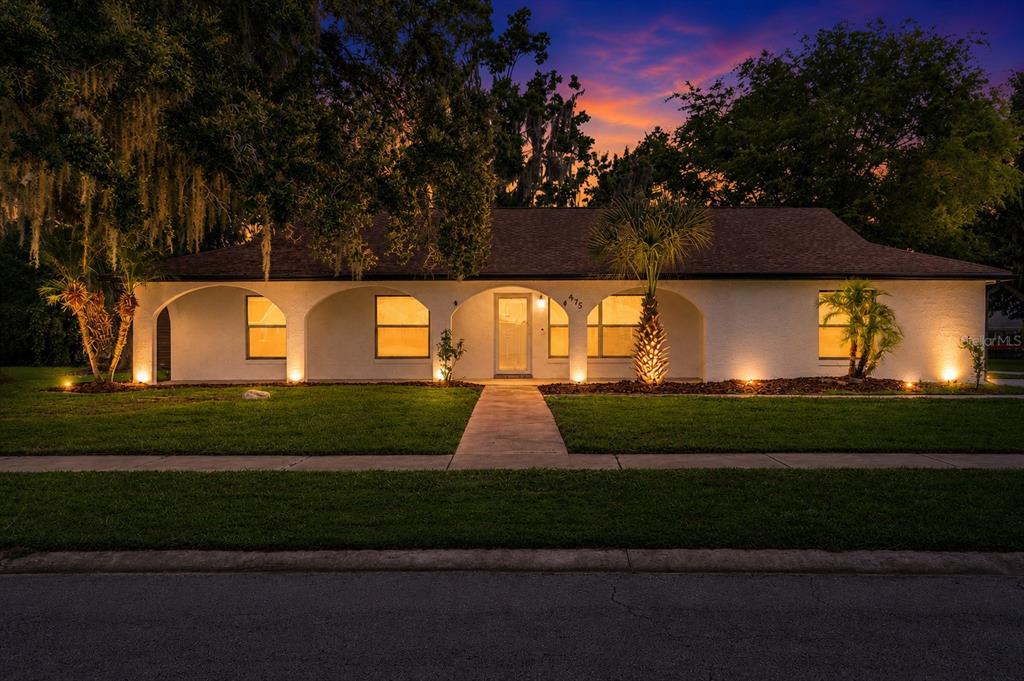 A single-story white house with arched entryways and illuminated windows at dusk — 475 WOODSTOCK DRIVE, PORT ORANGE, FL
