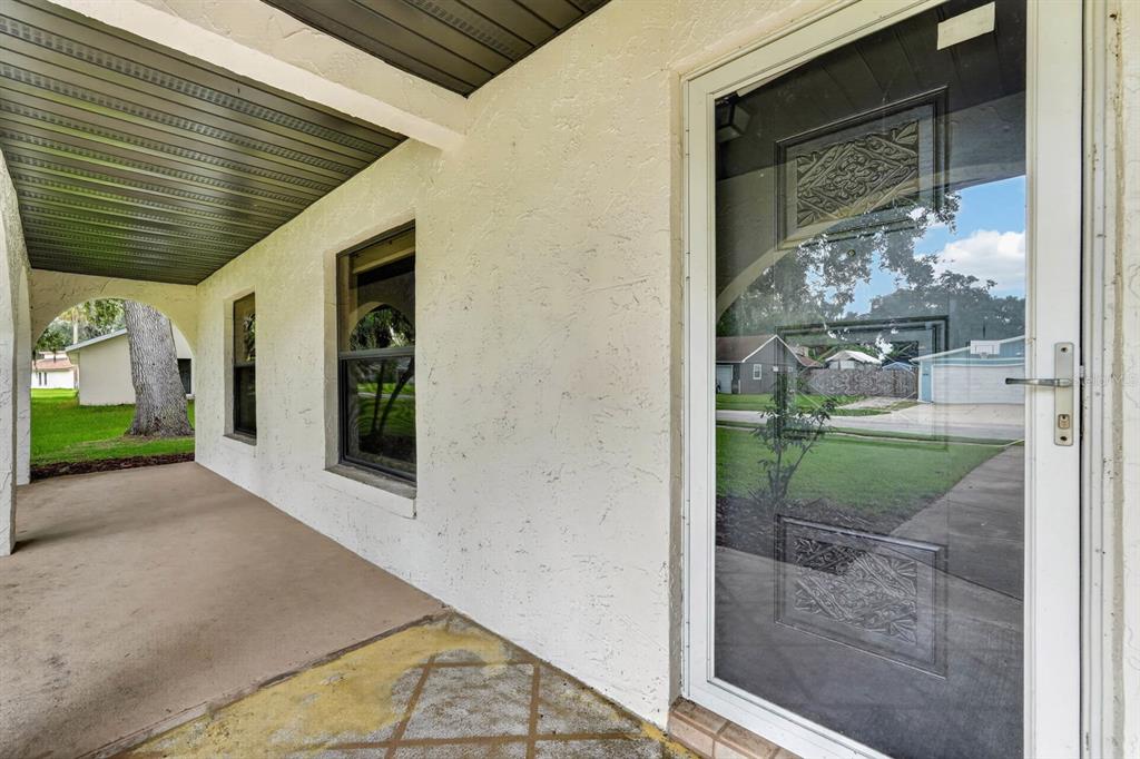 A covered concrete porch features a white stucco wall with two windows and a glass door — 475 WOODSTOCK DRIVE, PORT ORANGE, FL