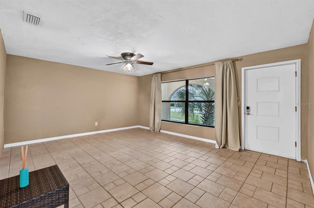 An empty room with tan walls, tile flooring, a ceiling fan, and a front door — 475 WOODSTOCK DRIVE, PORT ORANGE, FL