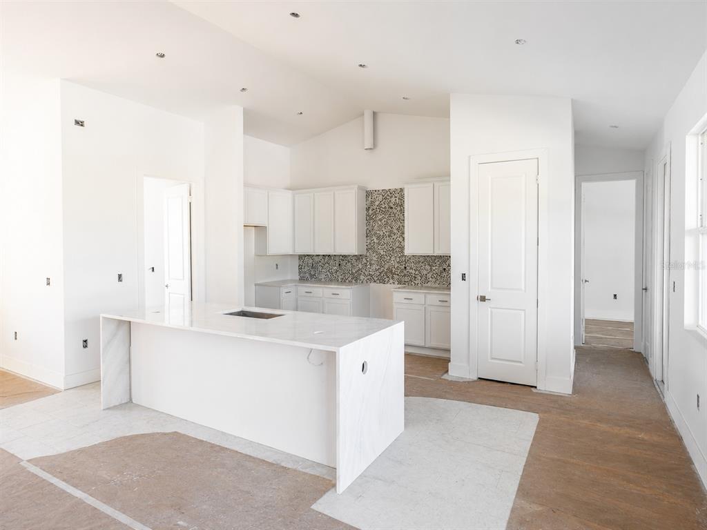 A modern kitchen features white cabinetry, a marble waterfall island, and a patterned tile backsplash — 142 FAIRWAY ROAD, ROTONDA WEST, FL