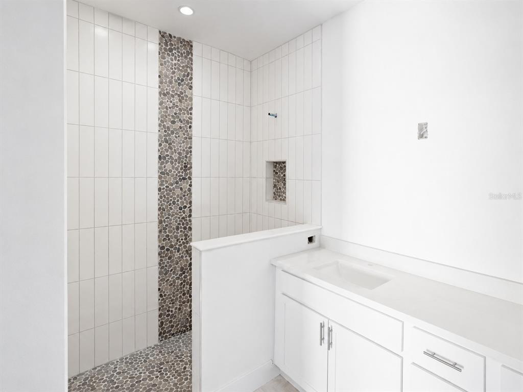 A bathroom features a walk-in shower with pebble tile accents and a white vanity — 142 FAIRWAY ROAD, ROTONDA WEST, FL