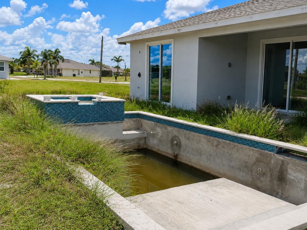 An unfinished swimming pool and spa sit in the backyard of a white house — 142 FAIRWAY ROAD, ROTONDA WEST, FL