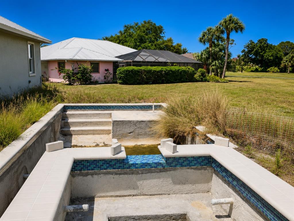 An unfinished concrete pool and spa structure sits in a backyard with a nearby house — 142 FAIRWAY ROAD, ROTONDA WEST, FL