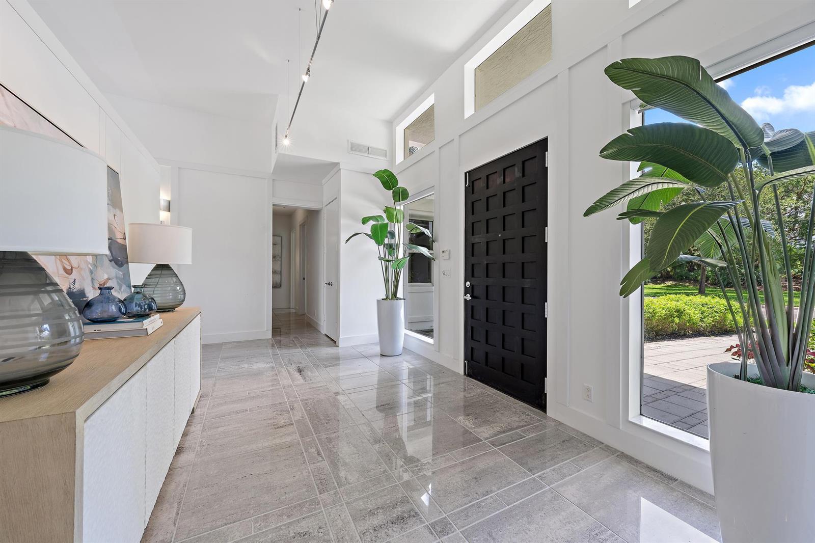 A bright entryway features white walls, a black paneled door, large potted plants, and tile flooring — 6070 Wildcat Run, West Palm Beach FL 33412, WEST PALM BEACH, FL