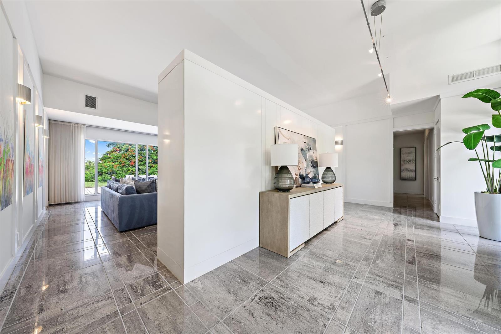 A white partition wall separates a tiled hallway from a living room with garden views — 6070 Wildcat Run, West Palm Beach FL 33412, WEST PALM BEACH, FL