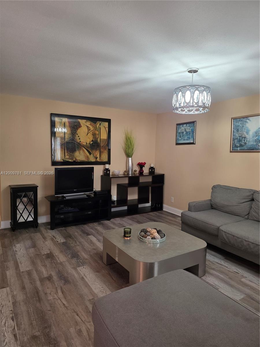 A living room features gray flooring, a gray sofa, a coffee table, and a chandelier — 232 E Saxony E # 232, Delray Beach FL 33446, DELRAY BEACH, FL