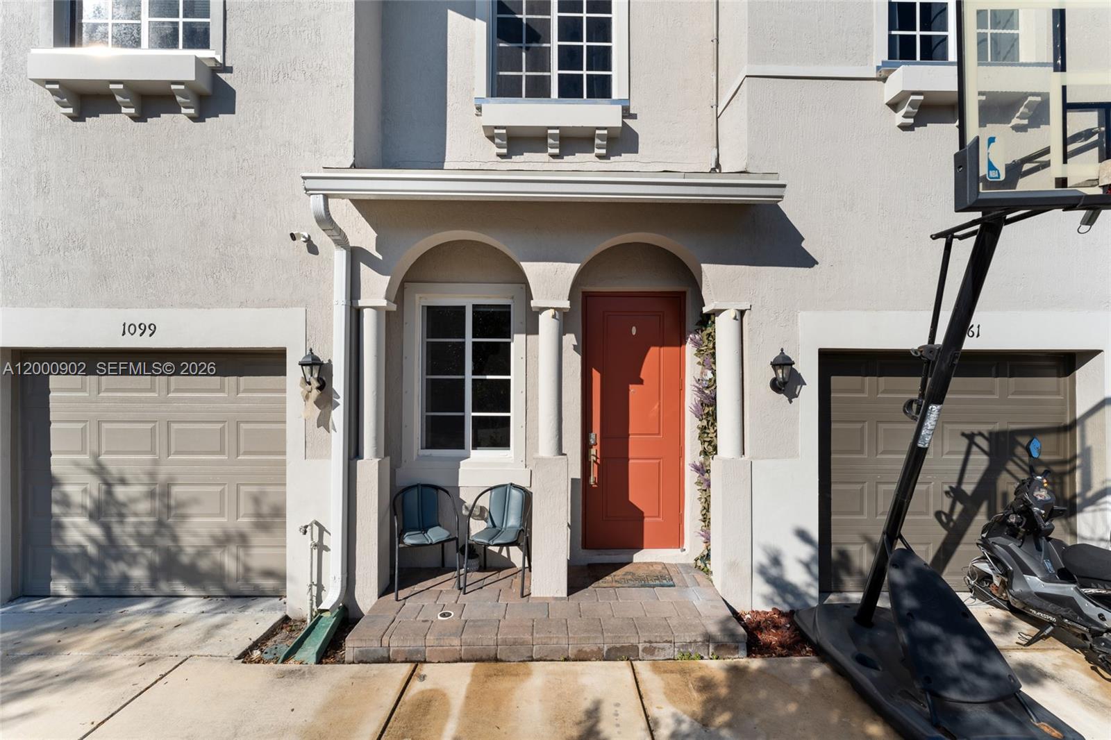 The exterior of a townhouse features a red front door, two chairs, and two garages — 1061 NW 208th Ter, Miami Gardens FL 33169, MIAMI GARDENS, FL
