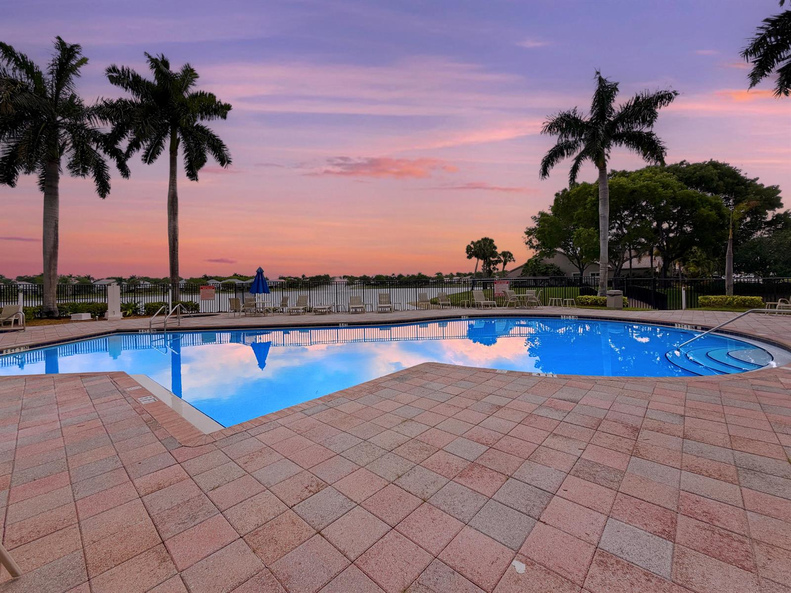 A swimming pool with a paved deck is surrounded by palm trees at sunset — 10725 Pelican Drive, Wellington FL 33414, WELLINGTON, FL