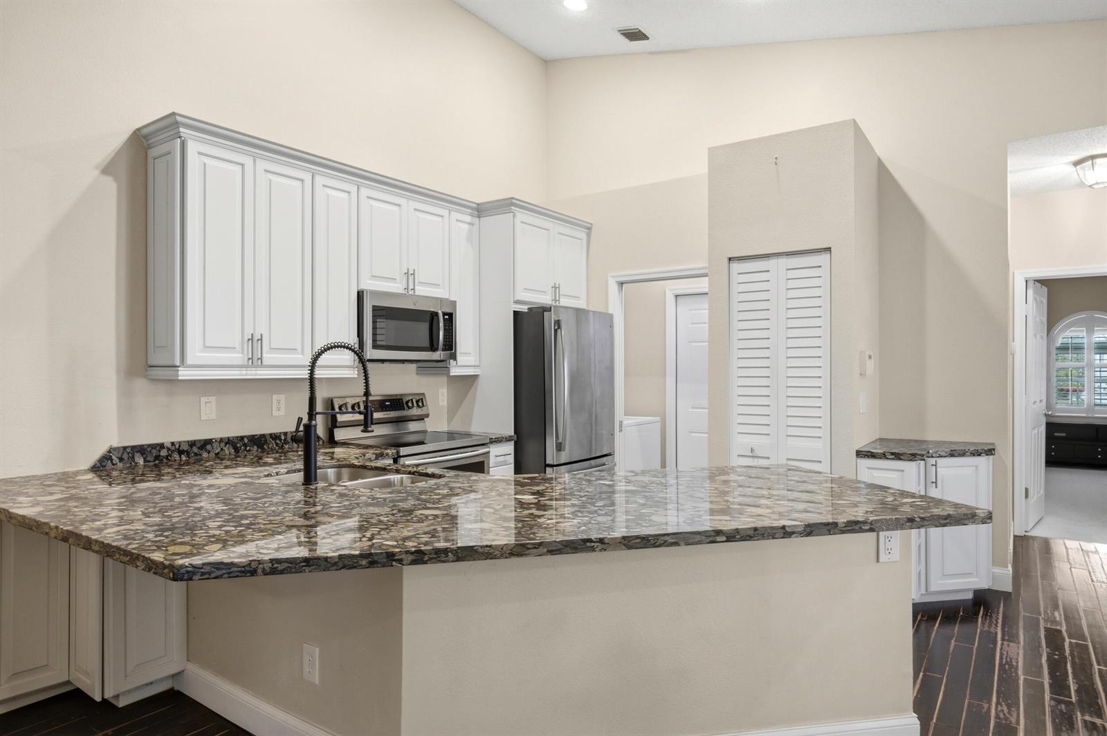 A kitchen features white cabinets, granite countertops, stainless steel appliances, and dark wood flooring — 10725 Pelican Drive, Wellington FL 33414, WELLINGTON, FL