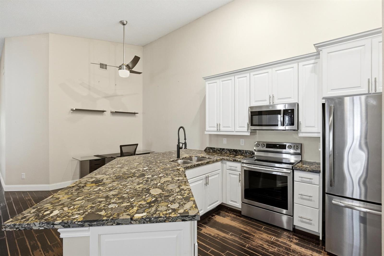 A kitchen with white cabinets, granite countertops, stainless steel appliances, and dark wood flooring — 10725 Pelican Drive, Wellington FL 33414, WELLINGTON, FL