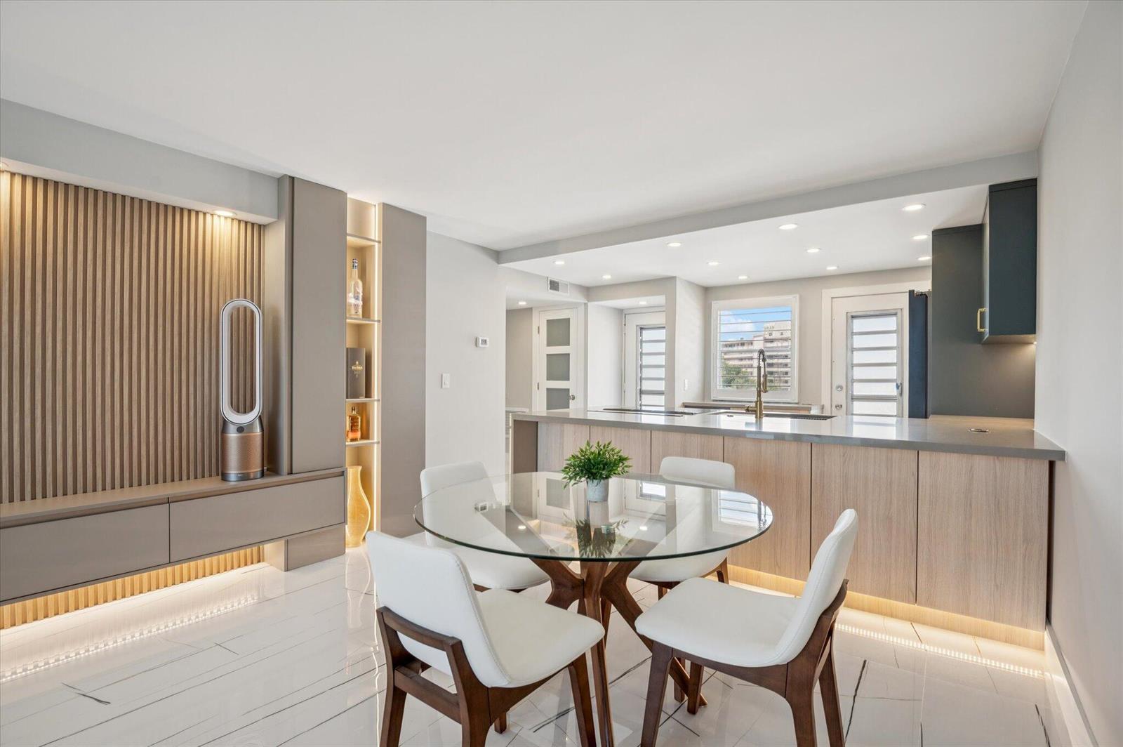 A modern dining area with a glass table, white chairs, and an adjacent kitchen island — 201 N Ocean Boulevard # 410, Pompano Beach FL 33062, POMPANO BEACH, FL
