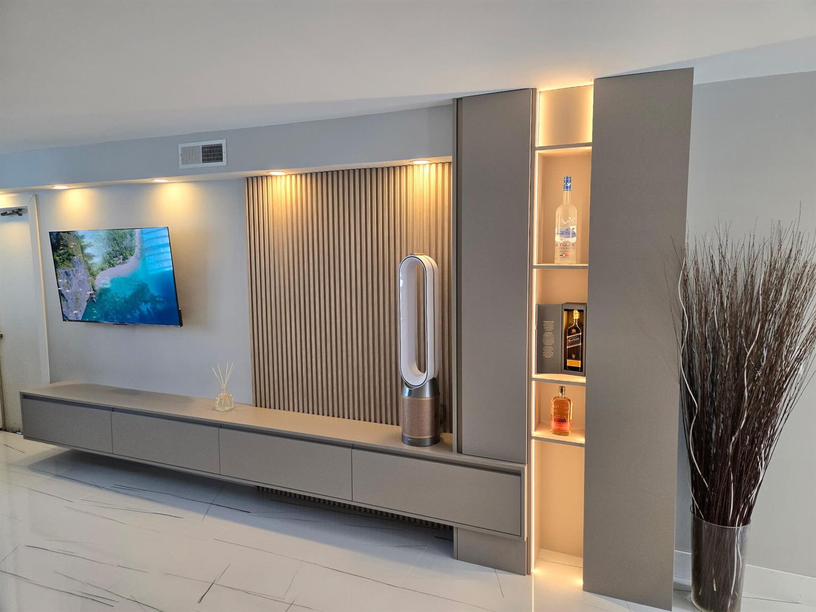 A modern living room features a wall-mounted television, slatted wood paneling, and illuminated display shelving — 201 N Ocean Boulevard # 410, Pompano Beach FL 33062, POMPANO BEACH, FL