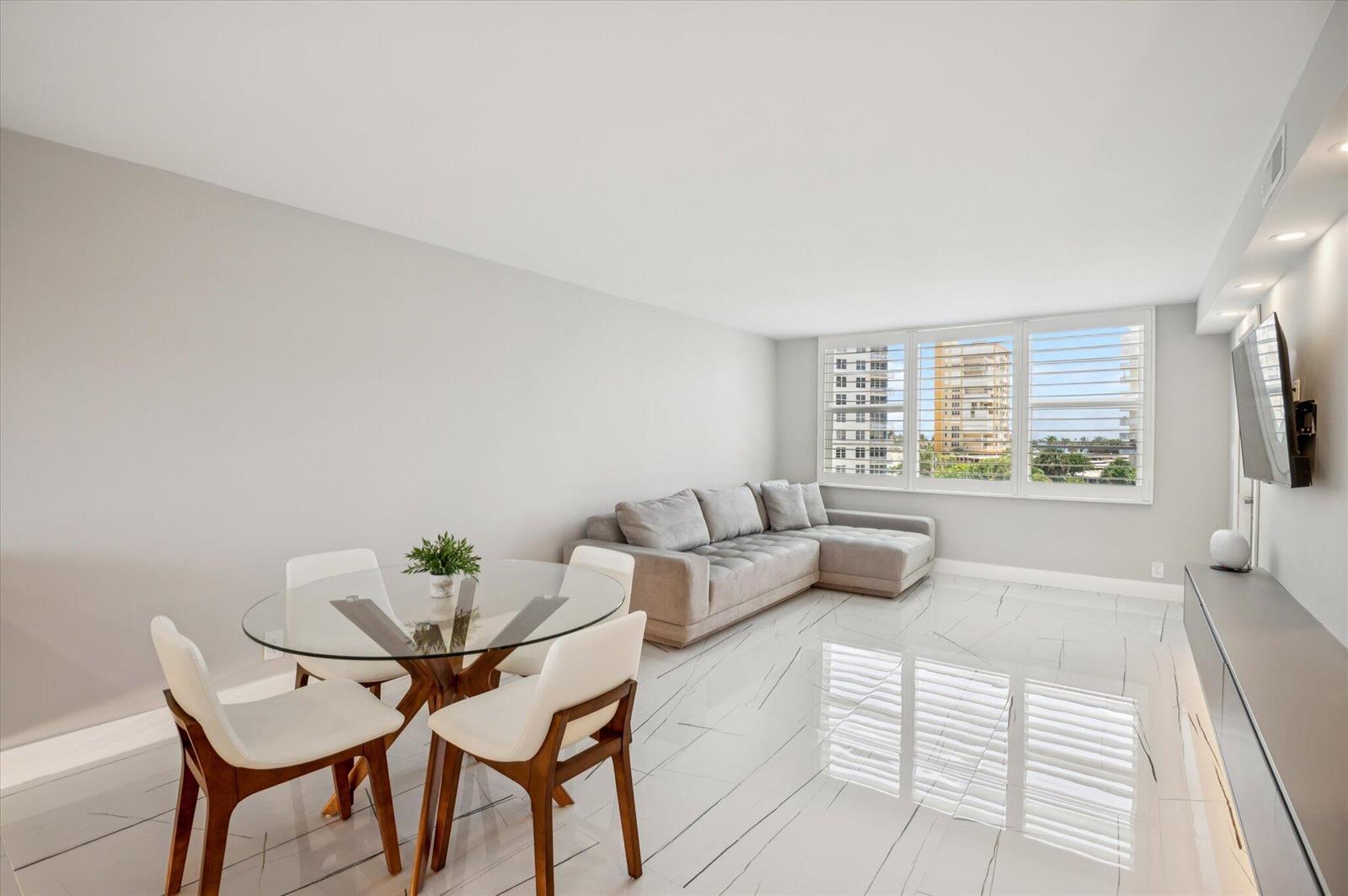 A living and dining area with white marble floors, a glass table, and a sectional sofa — 201 N Ocean Boulevard # 410, Pompano Beach FL 33062, POMPANO BEACH, FL