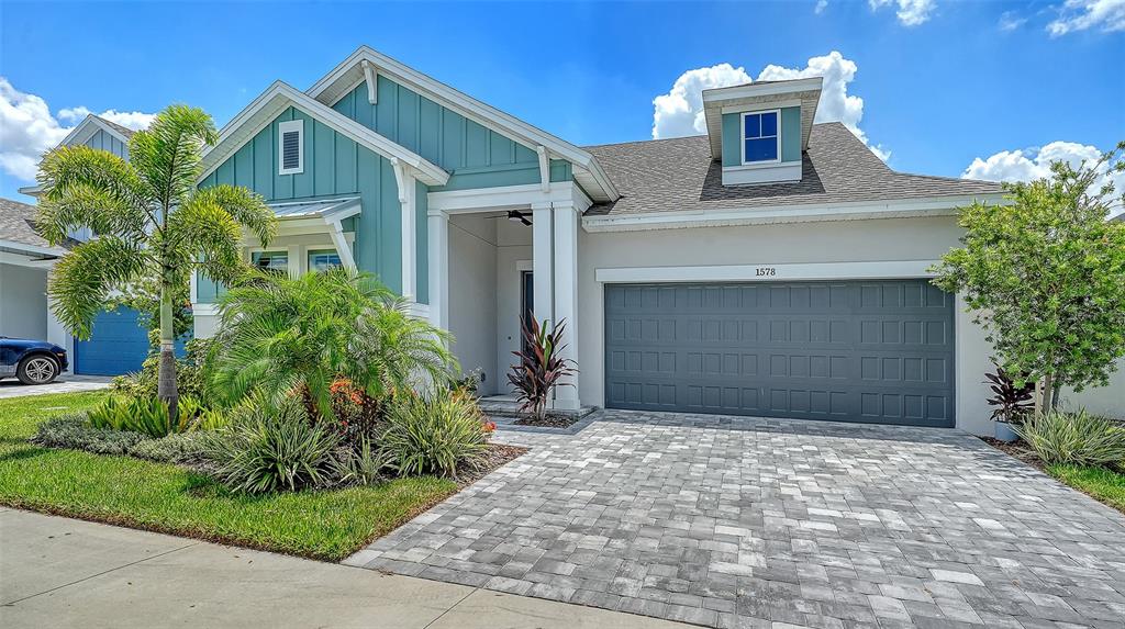 A single-story house with teal vertical siding, a gray garage door, and a paver driveway — 1578 RUNNING TIDE PLACE, SARASOTA, FL